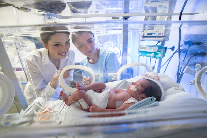 Loving mother and nurse at neonatal intensive care unit looking at the newborn baby in an incubator with oxygen with tenderness